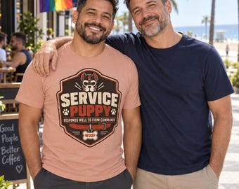 Könnte beinhalten: Ein altrosa T-Shirt mit einer Grafik eines Hundekopfes in einem Schild mit dem Text SERVICE PUPPY RESPONDS WELL TO FIRM COMMANDS und einem knochenförmigen Anhänger mit der Aufschrift WOOF, kombiniert mit einem dunkelblauen T-Shirt und beigen Hosen.