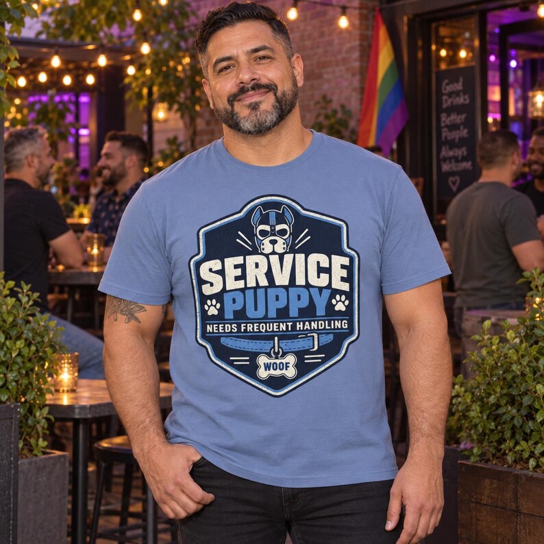 K&ouml;nnte beinhalten: Ein blaues T-Shirt mit einer Grafik eines Hundemasken-Motivs in Schildform, dem Text SERVICE PUPPY, NEEDS FREQUENT HANDLING und einem Hundehalsband mit einer Marke, auf der WOOF steht. Das Design enth&auml;lt Pfotenabdr&uuml;cke und blaue Akzente.