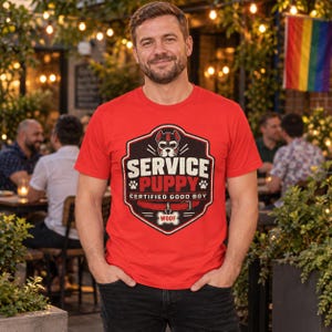 May include: A bright red short-sleeved t-shirt featuring a graphic emblem with a dog mask, the text "SERVICE PUPPY" and "CERTIFIED GOOD BOY", a red collar, and a bone-shaped tag with the word "WOOF" printed in the centre of the chest.
