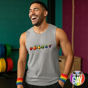Puede incluir: Una camiseta sin mangas gris con un diseño de frutas coloridas, que incluye una fresa, naranja, limón, lima, arándanos y uvas. El texto "Your Shirt Is GAY" está en una pegatina redonda. También se ve una pulsera arcoíris.