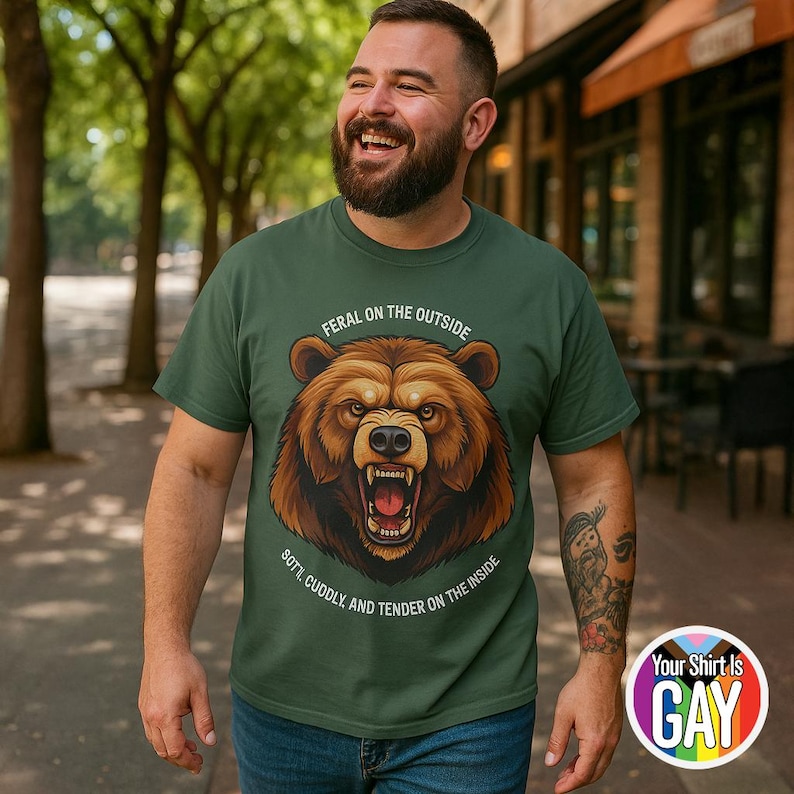 May include: Green t-shirt with a brown bear graphic. The bear is snarling, with the text "FERAL ON THE OUTSIDE, SOFT, CUDDLY, AND TENDER ON THE INSIDE." A rainbow circle with the text "Your Shirt Is GAY" is on the bottom right.
