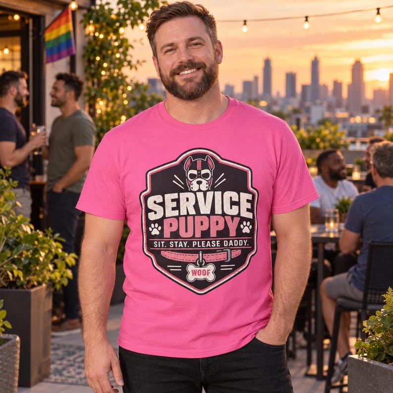 K&ouml;nnte beinhalten: Ein leuchtend pinkes T-Shirt mit einer schwarzen schildf&ouml;rmigen Grafik, die eine Hundemaske, den Text SERVICE PUPPY, den Satz SIT. STAY. PLEASE DADDY., ein rosa Halsband und ein knochenf&ouml;rmiges Schild mit dem Wort WOOF zeigt.