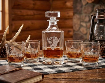 May include: A clear glass decanter and matching glasses set with a buffalo head design. The decanter is rectangular with a square stopper. The glasses are short and wide. The set is displayed on a black and white checkered cloth.
