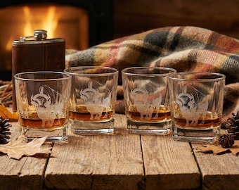 May include: Four square whiskey glasses with etched ram designs, filled with amber liquid, sit on a wooden surface. A leather flask and a plaid blanket are in the background, with a fireplace providing warm light.