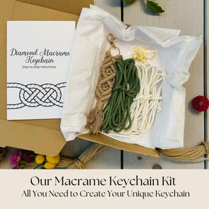 May include: A macrame keychain kit in an open cardboard box. The kit includes beige, green, and white cords, a gold-coloured keychain ring, and a printed instruction card. The card reads "Diamond Macrame Keychain" and "Step by Step Instructions."