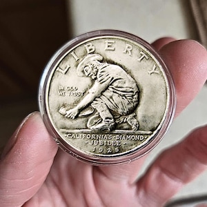 May include: A silver coin featuring a detailed relief of a prospector panning for gold. The coin is inscribed with "LIBERTY", "IN GOD WE TRUST", and "CALIFORNIA'S DIAMOND JUBILEE 1925". The coin is held in a clear protective case.