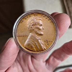 May include: A copper-colored 1914 S Lincoln cent coin, encased in a clear protective holder. The coin features a profile of Abraham Lincoln, with the inscriptions "IN GOD WE TRUST" and "LIBERTY".