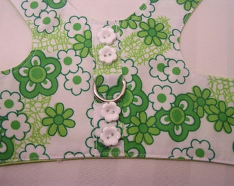 May include: White and green floral patterned pet harness with a metal ring and white flower-shaped buttons. The harness features a repeating pattern of green and white flowers on a white background, with a green trim.