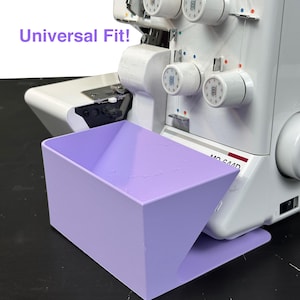 May include: A light purple overlock machine waste catcher. The text "Universal Fit!" is in the upper left corner. The overlock machine is white with several dials and thread spools. The waste catcher is rectangular with a sloped front.
