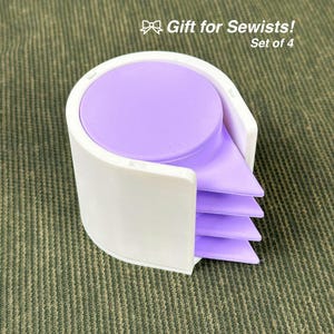 Może przedstawiać: Biało-fioletowy uchwyt na akcesoria do szycia z napisem "Gift for Sewists!" i "Set of 4". Uchwyt ma okrągłą górę i stos fioletowych trójkątnych elementów.