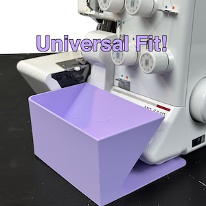 May include: A light purple sewing machine waste catcher with the text "Universal Fit!" is positioned in front of a white and gray serger. The catcher is rectangular with a flared opening. The serger has multiple thread spools.