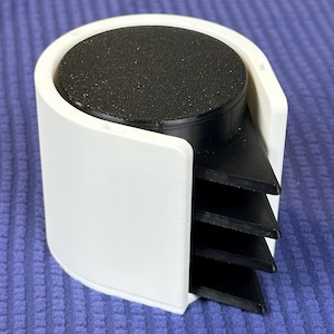 May include: A white and black coaster holder with four black coasters. The holder has a rounded design with a white exterior and a black interior. The coasters are triangular and fit neatly inside the holder.