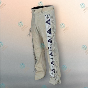 May include: Beige suede leather trousers featuring long fringe along the outer seams. A vertical panel on each leg displays a geometric pattern in white, dark blue, and green beads, incorporating cross shapes and triangles along the length.