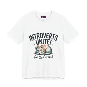 May include: White t-shirt featuring the text "Introverts Unite!" above a grumpy cartoon cat wearing a party hat. The phrase "(in the Corner)" is below the cat. The shirt has a crew neck and short sleeves.