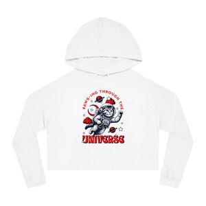 Puede incluir: Sudadera corta blanca con un diseño de gato astronauta, rodeado de planetas y estrellas. El texto "Paws-ing Through The Universe" está en rojo.
