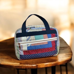 May include: A rectangular quilted pouch featuring a patchwork design of various fabric patterns including red and blue polka dots, stripes, and solid colors. It has a dark blue handle, a white zippered front pocket, and a top zipper closure.