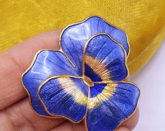 May include: A blue and gold enamel pansy flower brooch. The brooch features a detailed design with blue petals and gold accents. The flower is set against a yellow background.