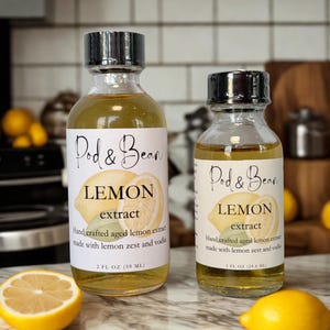 May include: Two glass bottles of lemon extract with black caps and white labels. The labels read "Pod & Bean LEMON extract" with a lemon illustration. The bottles contain a yellow liquid and are labeled 2 FL OZ (59 ML) and 1 FL OZ (29.6 ML).