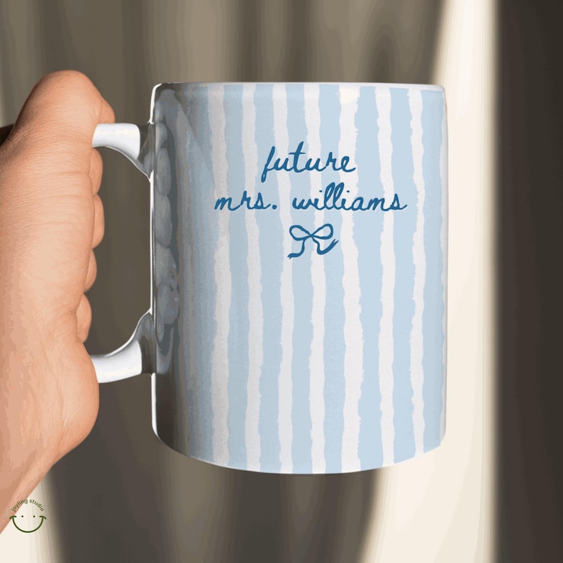 May include: White ceramic mug with a blue and white striped pattern. The mug features the text "future mrs. williams" in a handwritten font, along with a bow graphic. The mug has a white handle.