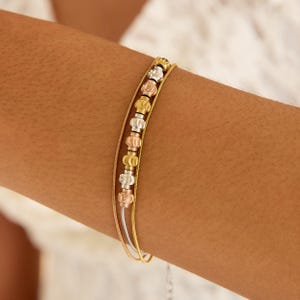 Könnte beinhalten: Ein mehrsträngiges Armband mit Gold-, Silber- und Roségoldtönen. Das Armband hat dekorative Perlen in Gold, Silber und Roségold. Das Armband wird am Arm einer Person getragen.