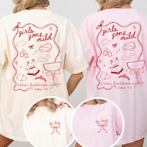 May include: Two t-shirts in cream and light pink featuring red line art. The back displays the text girls gone mild, Olivia's Bachelorette, Dallas, TX, with icons of a sleep mask, nail polish, pyjamas, a tiara, and a cocktail glass. The front has a bow.