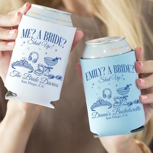 Könnte beinhalten: Zwei hellblaue Dosenkühler aus Schaumstoff mit dunkelblauem Text und Grafiken. Einer zeigt ME? A BRIDE? Shut Up! The Bride Diaries San Diego, CA. Der andere zeigt EMILY? A BRIDE? Shut Up! Diana's Bachelorette San Diego, CA. Beide zeigen Tiara und Ring.