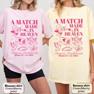 以下が含まれることがあります： ピンクと黄色の2枚のTシャツ。ピンク色の「A MATCH MADE IN HEAVEN」の文字。シャツには、天使、鳩、ハートのピンク色のグラフィックも描かれています。「Bianca's Bachelorette Miami, FL est. 2025」の文字が下に印刷されています。