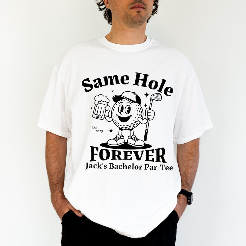 Puede incluir: Camiseta blanca con un gr&aacute;fico en blanco y negro. El gr&aacute;fico presenta un personaje de pelota de golf sosteniendo una cerveza y un palo de golf, con el texto "Same Hole Forever" y "Jack's Bachelor Par-Tee".