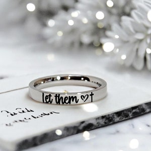 May include: A silver ring with the words "let them" and a heart symbol engraved on it.