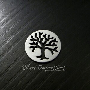 May include: A silver charm featuring a cut-out design of a tree. The charm is round and has a smooth finish.