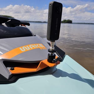 May include: A black Insta360 ONE X2 camera mounted on an orange metal bracket attached to a light blue and gray jet ski. The camera is positioned vertically with a silver and black ball head mount, featuring the text WAKE PRO on the jet ski hood.