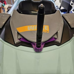 May include: A close-up of a jet ski's front section, featuring a black pole with a textured grip mounted on a purple bracket. The jet ski is gray and light blue, with the text "WAKE PRO" in yellow.