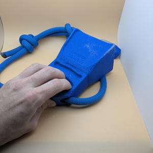 Puede incluir: Un agarre de escalada azul con una cuerda adjunta. El agarre tiene forma rectangular con el texto "Cowboy Climbing" impreso en el lateral. La cuerda es de color azul a juego y est&aacute; anudada en un extremo.