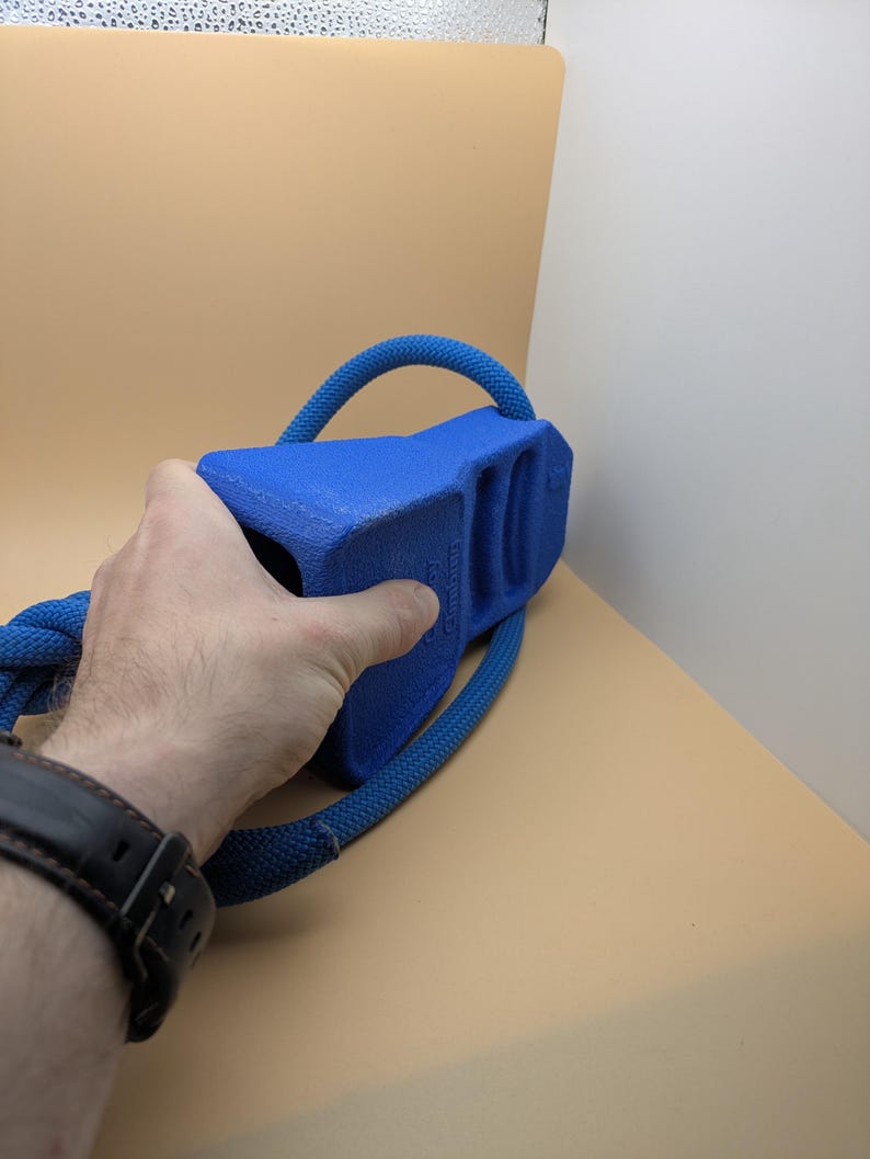 Puede incluir: Un juguete azul para perros con un asa de cuerda. El juguete tiene una forma rectangular s&oacute;lida con un asa curva hecha de cuerda azul. El juguete est&aacute; siendo sostenido por una persona.