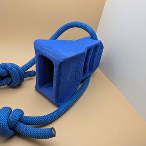 Puede incluir: Un calzo de rueda azul con un asa de cuerda. El calzo tiene una forma rectangular s&oacute;lida con un interior hueco. La cuerda es de color azul brillante y est&aacute; anudada en el extremo.