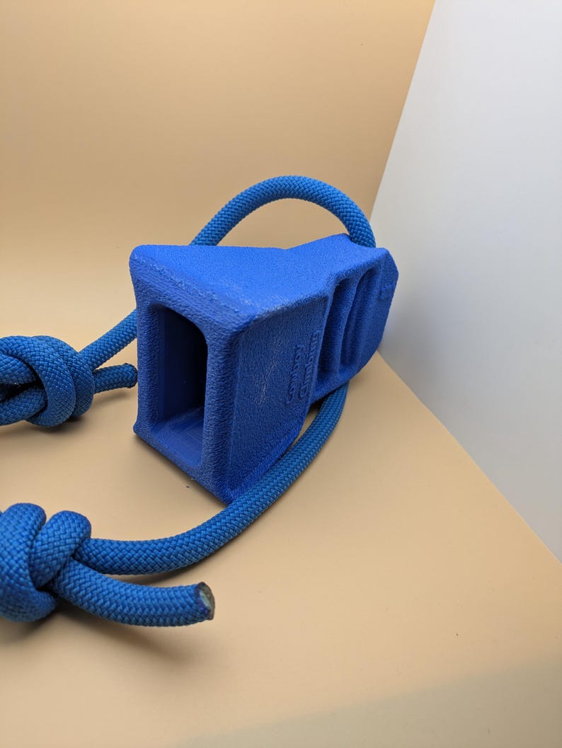 Puede incluir: Un calzo de rueda azul con un asa de cuerda. El calzo tiene una forma rectangular s&oacute;lida con un interior hueco. La cuerda es de color azul brillante y est&aacute; anudada en el extremo.