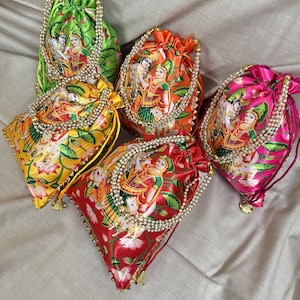 Puede incluir: Cinco bolsas de cordón de colores con un diseño tradicional indio que presenta una pareja en un entorno floral. Cada bolsa tiene un borde de perlas y una borla dorada.