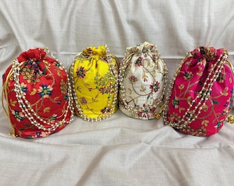 Può includere: Quattro sacchetti colorati con coulisse. I sacchetti sono rossi, gialli, bianchi e rosa, ognuno ornato da ricami floreali e un bordo di perle. I cordoncini sono dorati. I sacchetti sono disposti su uno sfondo di tessuto bianco.