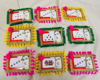 Può includere: Nove cornici decorative con accenti colorati. Ogni cornice presenta un ritratto di donna ed è adornata con nappe e un pompon. Le cornici sono in vari colori, tra cui verde, giallo e rosa, e sono disposte su una superficie bianca.