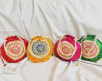 Può includere: Quattro borse rotonde colorate con coulisse, con ricami e abbellimenti intricati. Le borse sono rosse, gialle, rosa e verdi, ognuna con un design unico e un manico di perline. Le borse sono probabilmente utilizzate per trasportare piccoli oggetti.