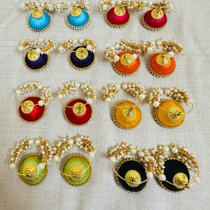 以下が含まれることがあります： カラフルな手作りのイヤリングのコレクション。各イヤリングは、青、赤、オレンジ、黄色、緑、黒など、さまざまな色で刺繍された丸いデザインが特徴です。金色のアクセントと小さな白い真珠のようなビーズで飾られています。