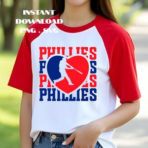 May include: A white baseball tee with red sleeves featuring the word "PHILLIES" in red and blue, with a baseball player silhouette inside a heart. The shirt also has the words "INSTANT DOWNLOAD PNG . SVG" in white.