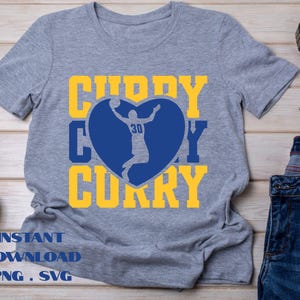 May include: A gray t-shirt with a blue heart-shaped graphic featuring a basketball player and the name "CURRY" in yellow. The text "INSTANT DOWNLOAD PNG . SVG" is printed at the bottom of the shirt.