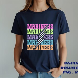 May include: Navy blue t-shirt with the word "MARINERS" stacked in a colorful, retro font. A black and white checkered lightning bolt graphic cuts through the text. The words "INSTANT DOWNLOAD PNG . SVG" are at the bottom.