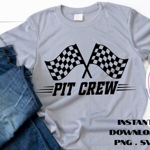May include: A light gray t-shirt featuring two crossed black and white checkered racing flags above the words "PIT CREW" in black. The shirt also includes the text "INSTANT DOWNLOAD PNG . SVG".