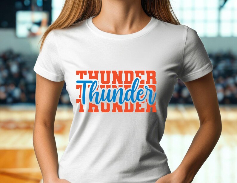 May include: White t-shirt with the word "Thunder" in orange block letters stacked vertically, with the word "Thunder" in blue script in the center. The shirt is short-sleeved and appears to be made of cotton.