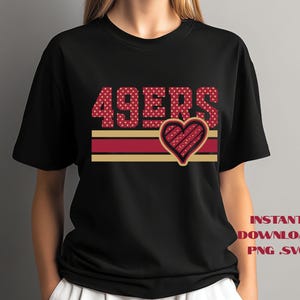 Peut inclure: T-shirt noir avec l'inscription "49ERS" en lettres à pois rouges et un motif de cœur. Le cœur est souligné en rouge et or, avec un motif rayé. Le t-shirt a un col rond et des manches courtes.