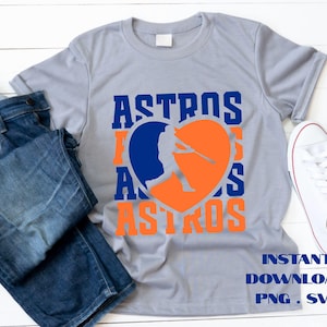 May include: Gray t-shirt with the word "ASTROS" in blue and orange. A baseball player silhouette is inside an orange heart. The text "INSTANT DOWNLOAD PNG . SVG" is at the bottom. Blue jeans and white sneakers are next to the shirt.