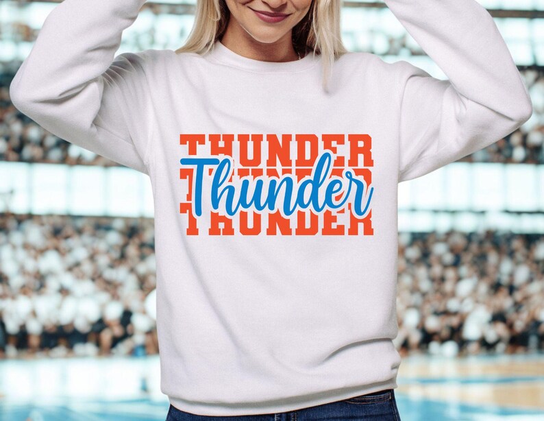 May include: White sweatshirt with the word "Thunder" in a stacked design. The top word and bottom word are in a bold orange font, while the middle word is in a blue script font.