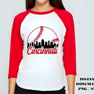 Könnte beinhalten: Ein weißes und rotes Baseball-Raglan-Shirt mit einem Baseball-Motiv und der Skyline von Cincinnati. Das Shirt hat rote Ärmel und einen weißen Körper. Das Wort "Cincinnati" ist in roter Schrift.